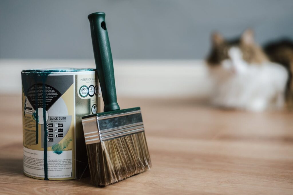 pexels-photo-4792527 Close-up of paint can and brush on floor with blurred cat in background.