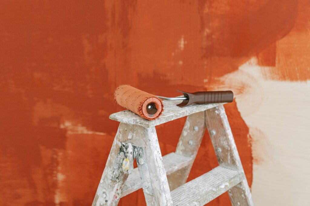 pexels-photo-5798984 Paint roller on a ladder with a partially painted red wall in the background.